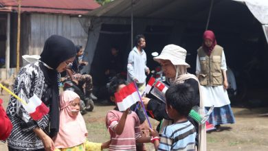 Relawan membagikan bendera kecil kepada anak-anak di pelosok Desa Tompu, Sigi, dengan latar tenda sederhana dan warga setempat.